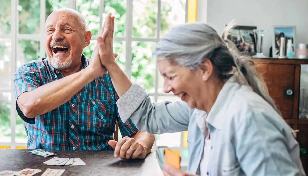 Two senior friends playing cards and laughing at assisted living community