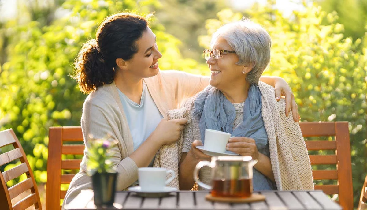 Daughter and elderly mother enjoying tea on an outdoor patio