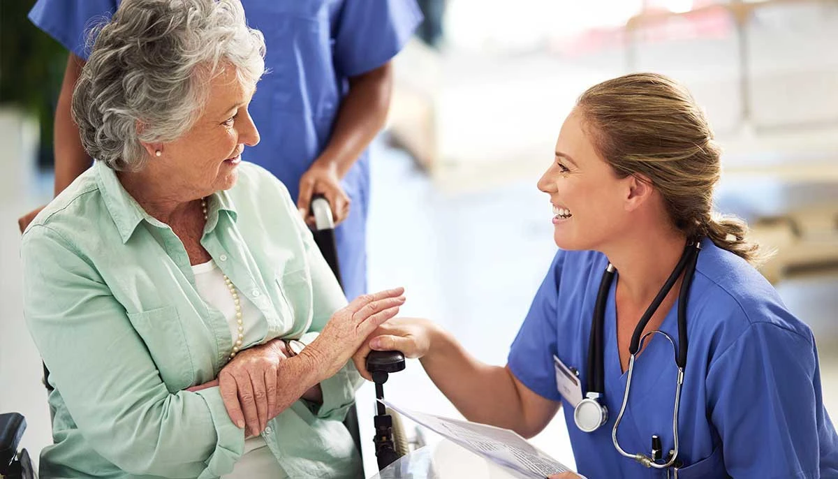 Senior woman in wheelchair talking to nurse in assisted living community