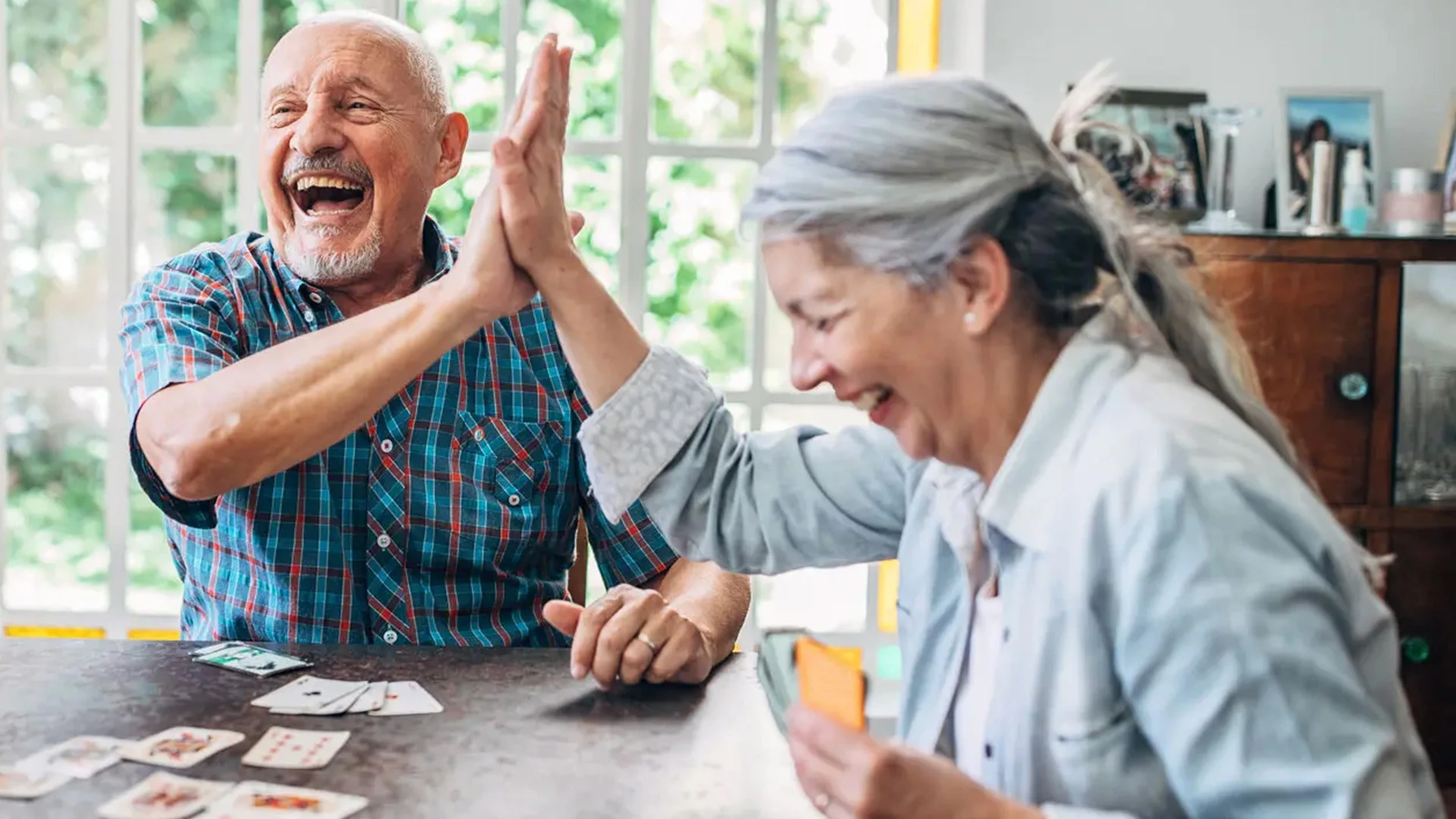 Two senior friends playing cards and laughing at assisted living community