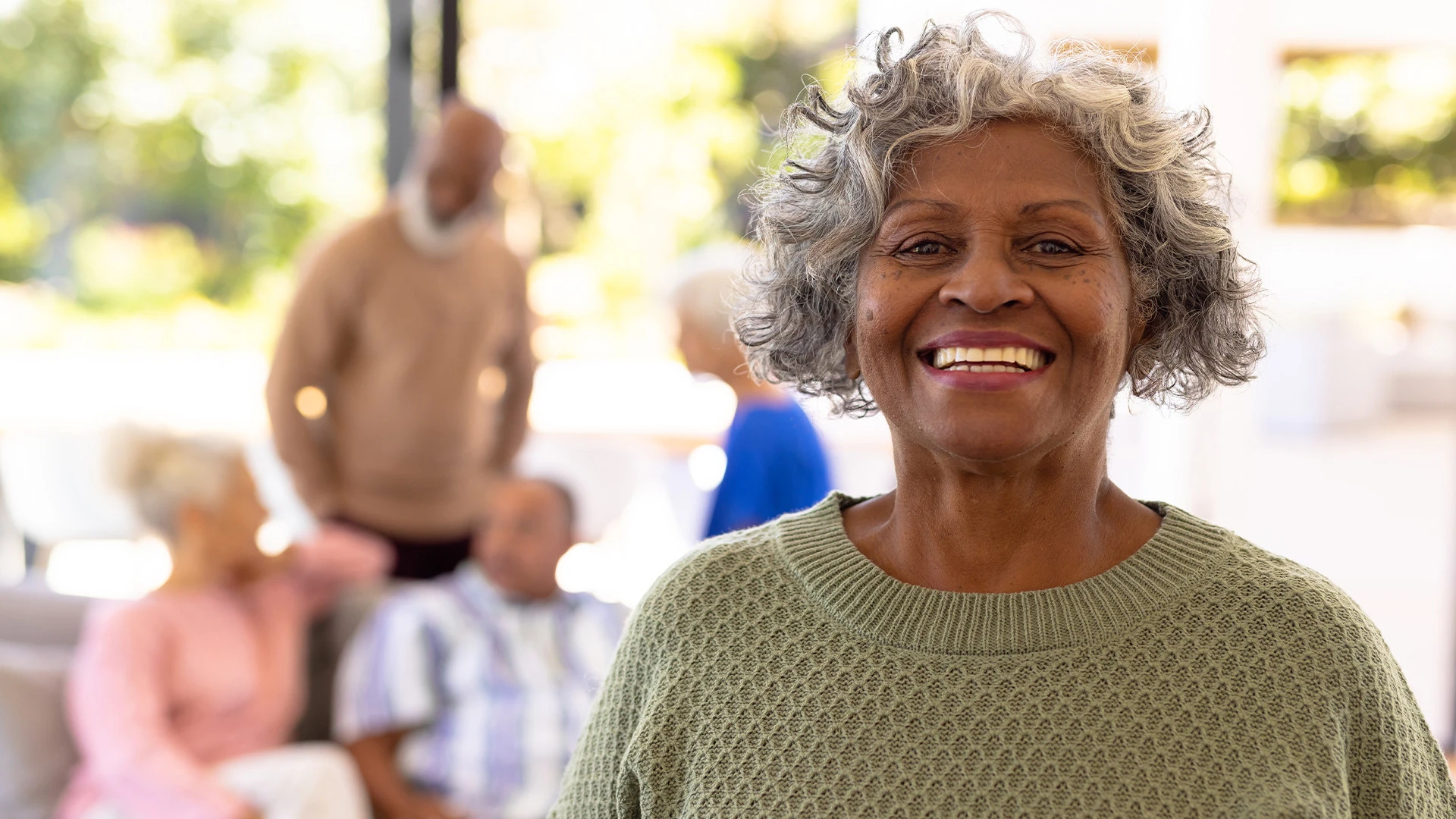 Elderly man in wheelchair drinking tea and talking to nurse in assisted living facility