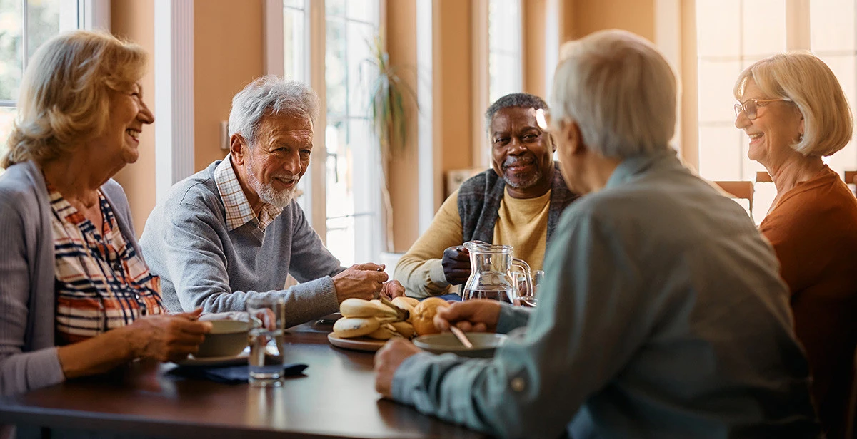 Group of senior friends enjoying breakfast and conversation at assisted living facility
