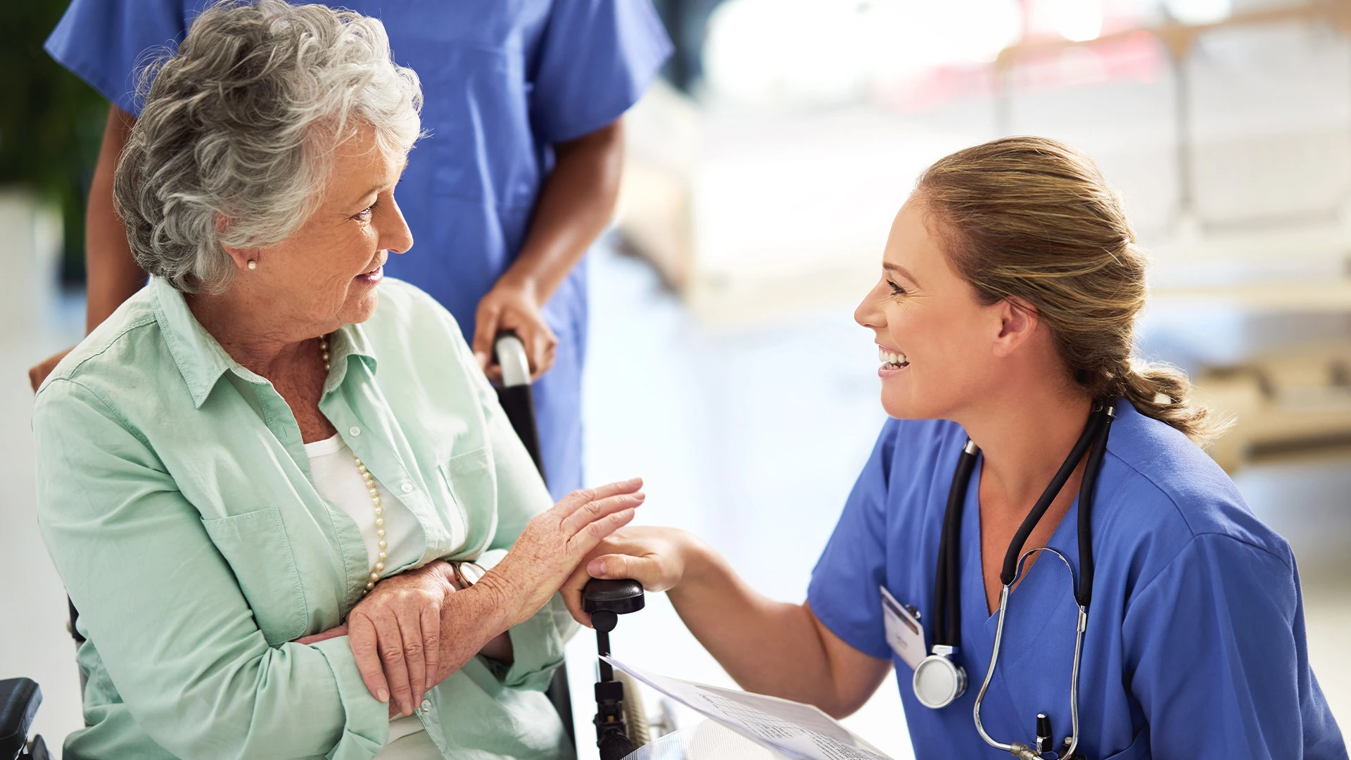 Senior woman in wheelchair talking to nurse in assisted living community